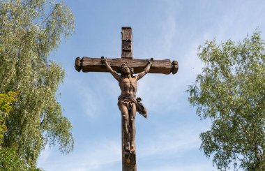 Hz. İsa 'nın heykeli mavi yaz gökyüzüne karşı iki ağacın arasında çapraz duruyor.