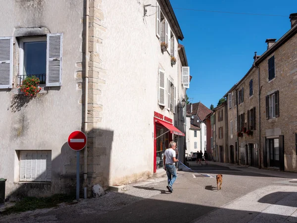 stock image orgelet, france, 10 august 2023: man walks dog on sunny street near old houses in french town of orgelet in jura