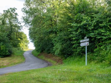 Çimenli ve ağaçlı kırsal yol mucizelere işaret eden işaretlerle dolu.