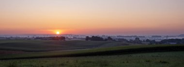 colorful sunrise and morning mist over distant germany seen from hill between groesbeek and nijmegen in the netherlands clipart