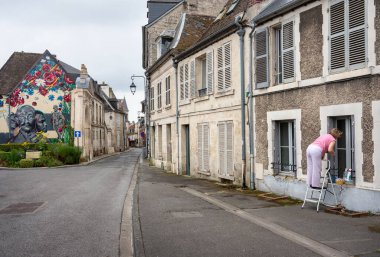 laon, france, 21 july 2024: woman in pink shirt cleans window in medieval city of Laon in the north of france clipart