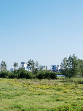 Mavi gökyüzü ve maasduinen çiçekleri arka planda wanssum endüstrisi ile nehir kenarı dolgusu üzerinde