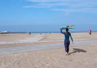 Wijk aan zee, Hollanda, 7 Eylül 2024: Hollanda sahillerinde sörf tahtası taşıyan kadın denize doğru yürüyor