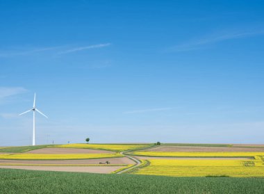 Baharda mavi gökyüzünün altında rüzgâr türbini bulunan Lüksemburg 'da tarım arazisi