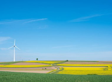 Baharda mavi gökyüzünün altında rüzgâr türbini bulunan Lüksemburg 'da tarım arazisi