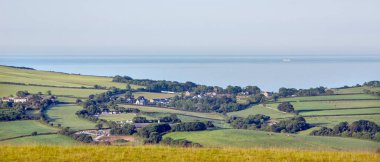Güney Devon 'daki çayırlar ve köy. Arkasında mavi deniz olan bir gemi.