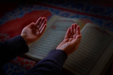 İslami fotoğraf. Elleri havada dua eden müslüman adam. Arka planda kutsal Kur 'an. Ramazan veya İslami konsept fotoğraf. Seçici odak.