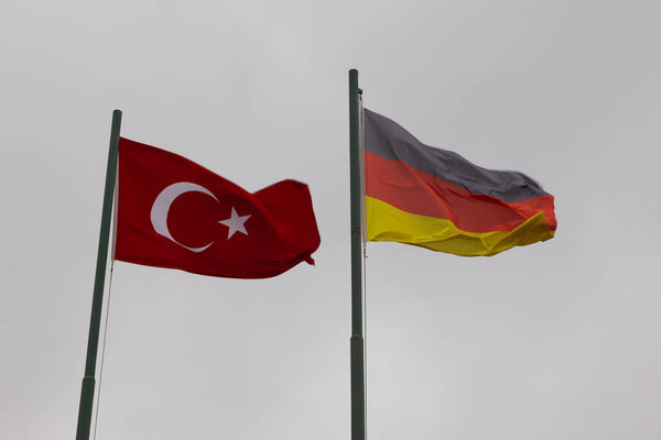 German and Turkish flags on the flagpole with overcast sky on the background. Germany and Turkiye agreement or partnership or competition concept background.