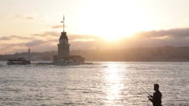 Kiz Kulesi ya da Bakireler Kulesi gün batımında bir balıkçıyla birlikte. İstanbul 4K videosu. İstanbul Türkiye - 6.7.2023