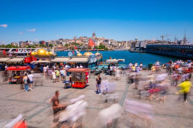 Eminonu Meydanı 'nda insanlar, yemek arabaları ve tekneler var. Arka planda Galata Kulesi var. İstanbul Türkiye - 6.8.2024