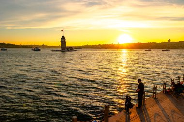 Kiz Kulesi ya da Maiden 's Tower manzaralı gün batımında etrafı gezen insanlarla. İstanbul Türkiye - 6.8.2024