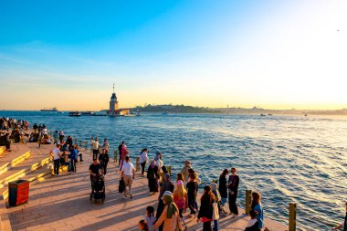 İstanbul konsept fotoğrafını ziyaret edin. Bakire Kulesi, nam-ı diğer Kiz Kulesi ve günbatımında insanlar. İstanbul Türkiye - 5.18.2024