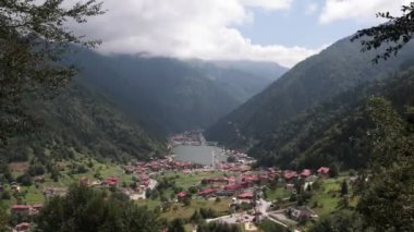 Tepeden Trabzon Uzungol manzarası ve arka planda orman kaplı dağlarla parçalı bulutlu gökyüzü