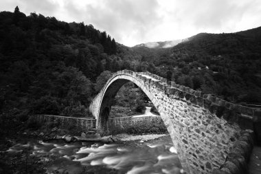 Stone bridge on the stream in a forest. Senyuva Bridge in Rize Turkey. Black and white photo of an old bridge. clipart