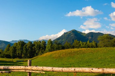 Çayır ve orman dağlarla kaplıydı. Ahşap çit ve kırsal alan manzarası. Tarım alanı ya da çayırlık.