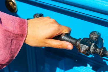 Elinde mavi kapının klasik metal kapı kolu tutan bir kadın. Kapıyı açıyorum..