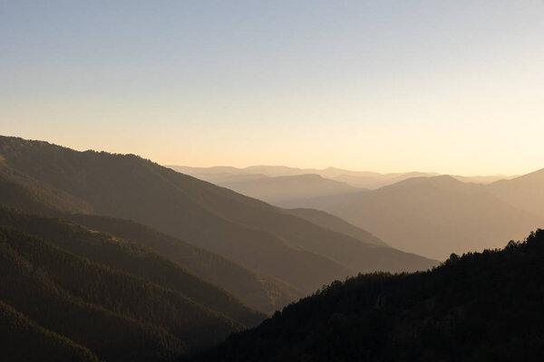 Landscape of the hazy mountains at sunset or sunrise. Layered hills and clear sky background photo.