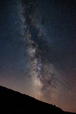 Samanyolu ve tepenin silueti. Yıldızlı gece arkaplanı dikey fotoğrafı.