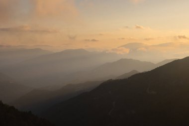 Gün batımında sisli ve bulutlu puslu dağ sıraları. Dağ sırası manzarası.
