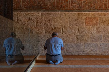 Muslim man praying in the mosque and his reflection on the glass in Great Mosque of Divrigi aka Divrigi Ulu Camii. Sivas Turkey - 6.26.2024 clipart