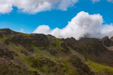 Parçalı bulutlu gökyüzü ve yazın yuvarlanan bulutlarla dağların manzarası..