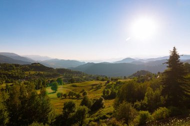 Yazın arka planında çayır ve dağ sıraları olan kırsal alanın manzarası.