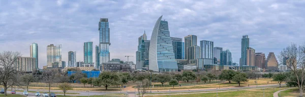 stock image Views from Butler Metro Park of Austin Texas cityscape. Panoramic view of the park with trees, parking spaces, and pathways at the front of the skyscraper buildings against the cloudy sky.