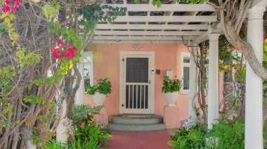 La Jolla, California 'daki bir evin Panorama Red beton girişi. Beyaz bir pergola çatısı var. Yan taraflarında saksı bitkileri olan beyaz ön kapıya giden yolun üzerinde begoninvillea var..