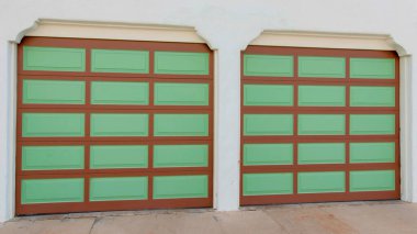 La Jolla, Kaliforniya 'da kahverengi çizgili ve yeşil panelli iki garaj kapısı. Şık kapı çerçeveleri ve beton döşemeleri olan garaj dış tarafı..