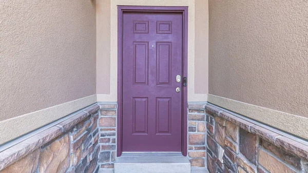 Panorama Purple front door with arched transom window and digital key access. Entrance of a house in the middle of the walls with stone veneer sidings and a security camera near the door.