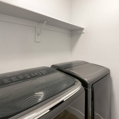 Çamaşır odasında yansıtıcı camlı ikinci kare çamaşır aletleri. Süslü çamaşır makinesi ve kurutma makinesi rafın altında, beyaz duvarda deste var..