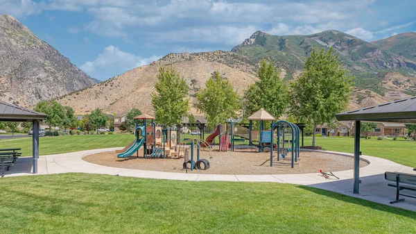 stock image Panorama White puffy clouds Public park at Utah Valley with playground in the middle. There are two pavilions on both sides with picnic table in a residential area with a view of mountains at the back.