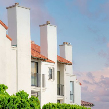 Gün batımında Kare Kabarık Bulutlar La Jolla, California 'daki Beyaz Konut Binası. Bacaları, pencereleri ve balkonları açık gri gökyüzüne karşı olan bir binanın dış cephesi..