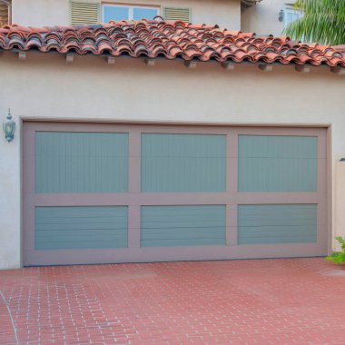 La Jolla, California 'da kırmızı tuğlalı bir garaj kapısı var. Açık kahverengi çerçeveleri ve gri panelleri olan garaj dışı ve solda bitkileri olan bir kapı manzarası..