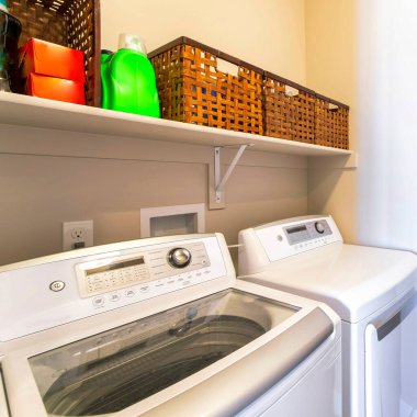 Çamaşır yıkama yerleri ve karanlık ahşap depolama dolapları olan küçük bir çamaşırhane. Rafın üstünde dokuma sepetler var. Masa dolabının yanında sağdaki çekmecenin yanında.