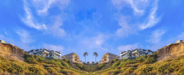 Abstract mirrored background Low angle view of a mountain slope with wild plants and buildings on top at San Clemente, CA. There are two apartment buildings on the left with balconies against the sky