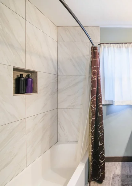 洗面台とバスタブ付きの垂直狭いバスルームのインテリア 正面の壁には 窓の近くにタオル 花瓶がある花崗岩のカウンターの上に額鏡があります — ストック写真