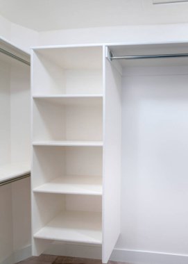 Dolabın içinde dikey beyaz raf birimleri var. Üstünde plastik destekler, metal çubuklar ve ön duvarda dikey çerçeveli raflar olan raflar var..