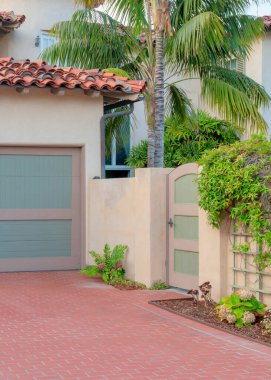 La Jolla, California 'da kırmızı tuğlalarla kaplı dikey garaj. Açık kahverengi çerçeveleri ve gri panelleri olan garaj dışı ve solda bitkileri olan bir kapı manzarası..