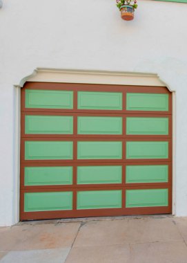 La Jolla, Kaliforniya 'da kahverengi çizgileri ve yeşil panelleri olan dikey iki garaj kapısı. Şık kapı çerçeveleri ve beton döşemeleri olan garaj dış tarafı..