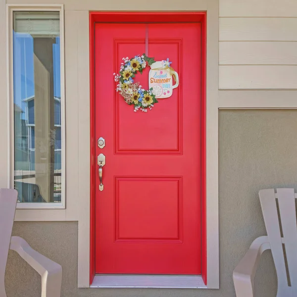 Stock image Square Entrance exterior of a house with two armchairs and red front door with wreath. Front porch exterior of a house with doormat and railings against the view of the neighborhood building.