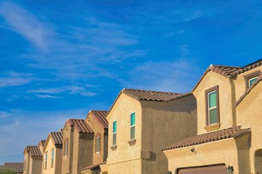 Tucson, Arizona 'da bir banliyö mahallesindeki evlerin yan görüntüsü. Boyalı bronzlaşmış sıva duvarları ve gökyüzüne karşı kil çatı kiremitleri olan özdeş evler.
