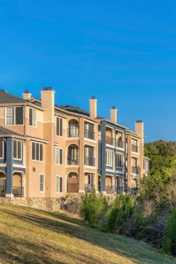 Austin, Teksas. Austin Gölü 'nün yakınındaki çimenli bir yamacın tepesinde üç katlı bir apartman. Mavi gökyüzüne karşı ağaçların yanında balkonları olan bir bina manzarası.