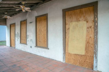 San Antonio, Texas- Exterior of an abandoned house with boarded doors and windows. Old house porch with red tiles flooring under a wooden roof ceiling with old fans. clipart