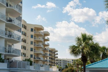 Destin, Florida... Balkonlu apartman manzaralı. Parlak gökyüzünün altında palmiye ağaçları olan apartmanları olan bir mahalle..