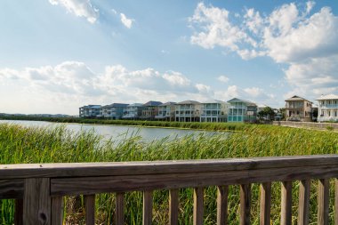 Destin, Florida- uzun çimen bitkileri ve üç katlı evlerle çevrili bir göl manzarası. Göl kenarındaki yerleşim yerleri ve bitkiler tahta korkuluklardan görünür..