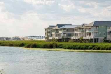 Destin, Florida- göl manzaralı teraslı konut binaları. Cephede bir göl var. Evlerin yakınında çimen bitkileri var. Gökyüzüne karşı ve arkada köprü var..