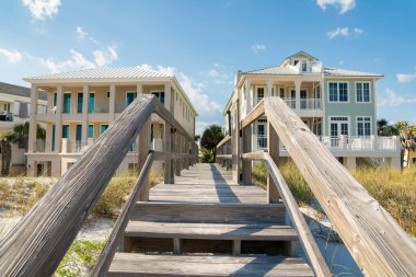 Destin, Florida... Sahildeki evlerin önündeki kum tepelerinin üstündeki tahta yaya köprüsüne basıyor. Teraslı binaların arasında raylı bir yol var..