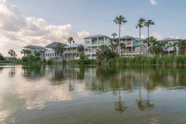 Destin, Florida- Göl manzaralı teraslı evler. Cephede bir göl var. Yansıtıcı su ve kıyıda uzun otlar var. Gökyüzüne karşı büyük yerleşim yerlerinin yakınında..