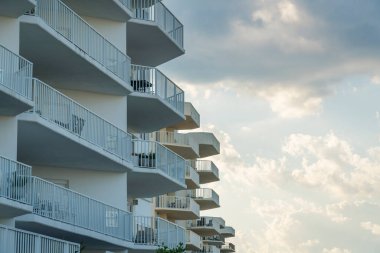 Destin, Florida 'daki her balkonda kahve masası ve sandalyeli bir sıra daire. Gökyüzündeki bulutlara karşı apartman binalarının alçak açılı görüntüsü.